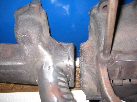 1953 Ford Mainline - Close-up view of two automotive exhaust manifolds, showing their cast iron construction and mounting points.