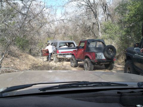 1996 Ford Bronco - Shot through a dusty windshield over the hood and wiper of the photographer's truck, looking down a brushy trail at a red-and-white lifted…