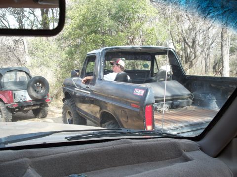 1996 Ford Bronco - Seen through the photographer's windshield on a wooded trail, a black square-body two-door 4x4 runs with its top removed, exposing a bare r…