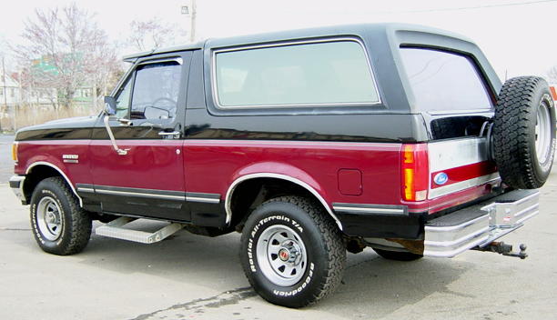 Rear three-quarter view of black and dark red Ford Bronco SUV with rear spare tire and white-letter tires