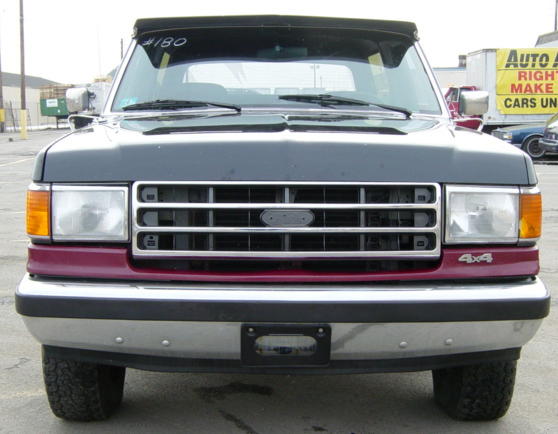 Front of a black and maroon two-tone Ford Bronco with chrome grille and 4x4 badge in a paved lot