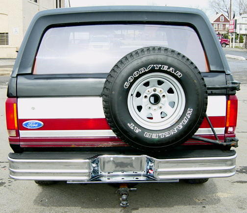 Rear of a maroon and silver Ford Bronco with hardtop and rear-mounted Goodyear Wrangler spare tire