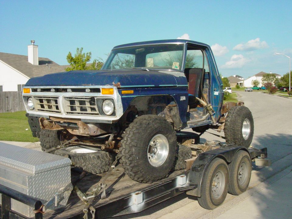 Blue Ford pickup truck body on a trailer with large off-road tires