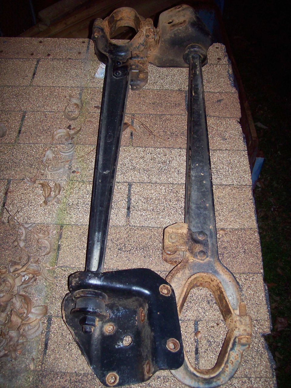 Two old, black metal truck suspension parts on a shingled surface.
