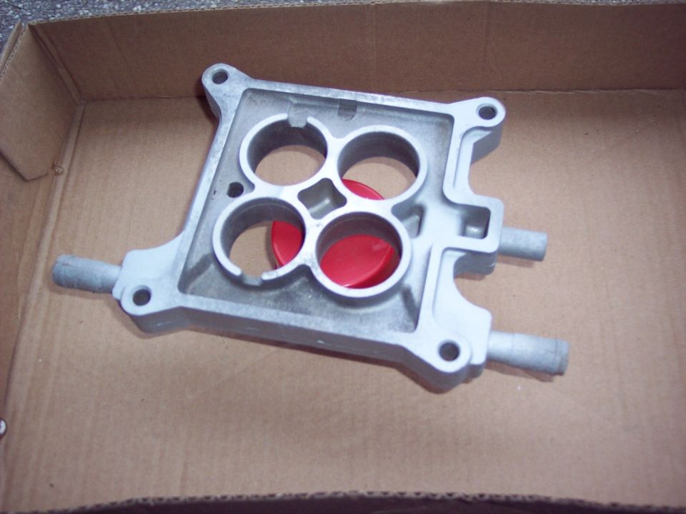 Silver aluminum intake manifold with red caps inside a cardboard box.