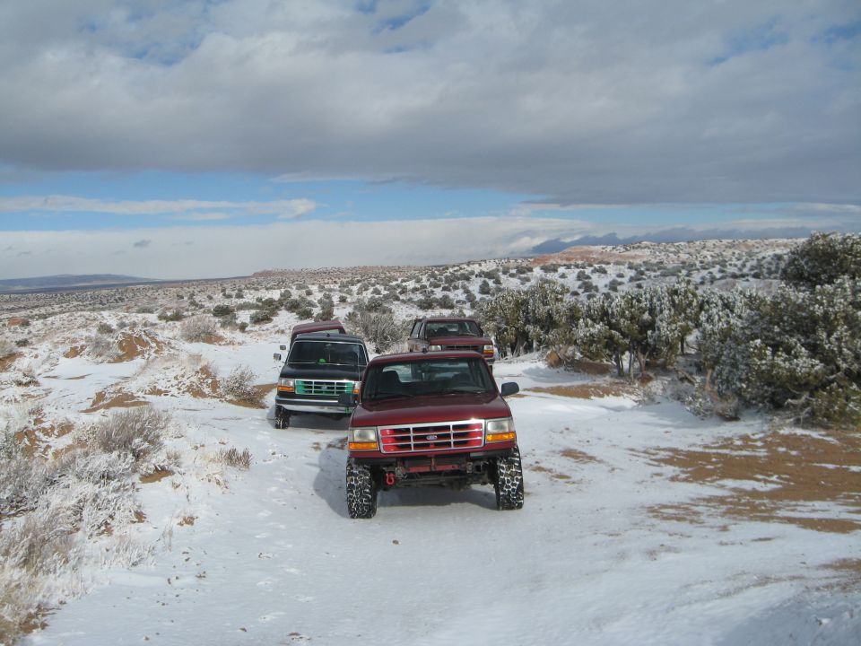 Three Ford trucks parked in a snowy desert landscape.