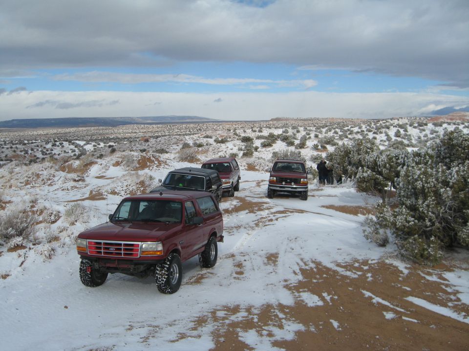 Red 1993 Ford Bronco in a snowy desert landscape with other SUVs.