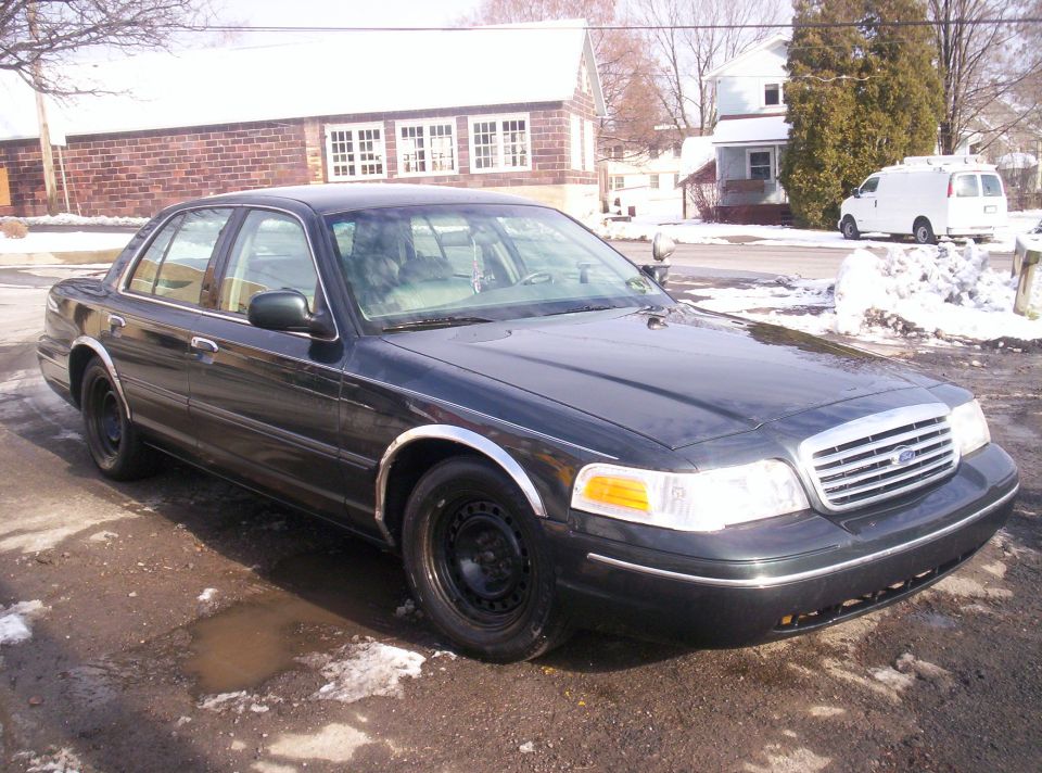 1999 Ford Crown Victoria sedan, dark green, parked on a wet road with snow.