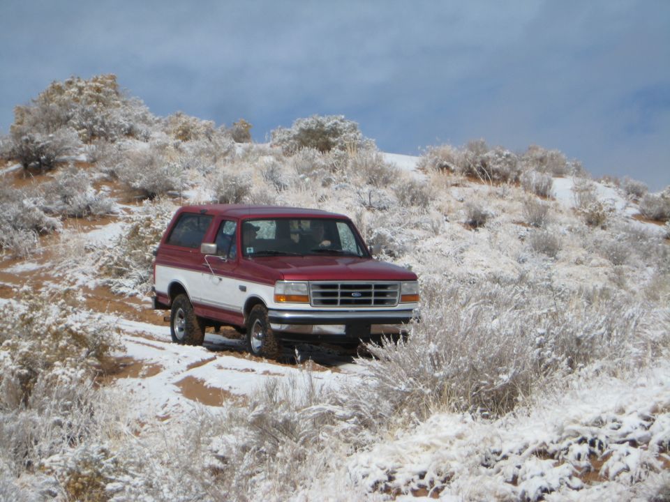 Red and white Ford Bronco on a snowy desert trail.