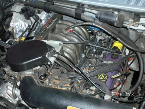 1996 Ford Bronco - Close-up view of the engine bay of a 1996 Ford Bronco, showing the intake manifold, air filter housing, and various hoses and wiring. The d…