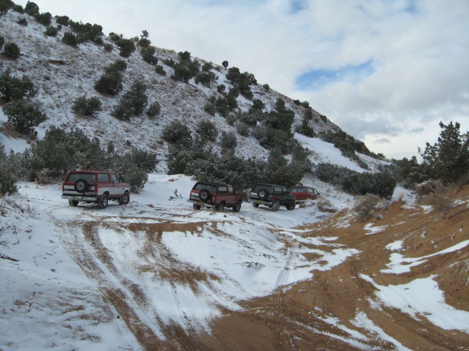 SUVs parked on a snowy trail on a hillside.
