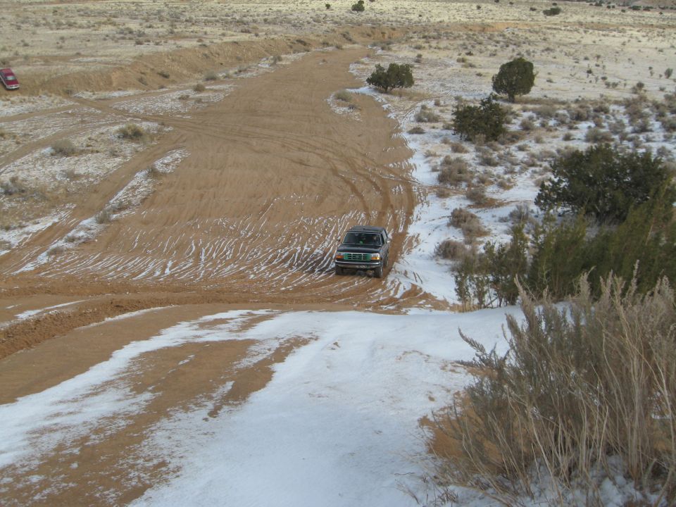Dark green Ford Bronco driving down a sandy hill with patches of snow.