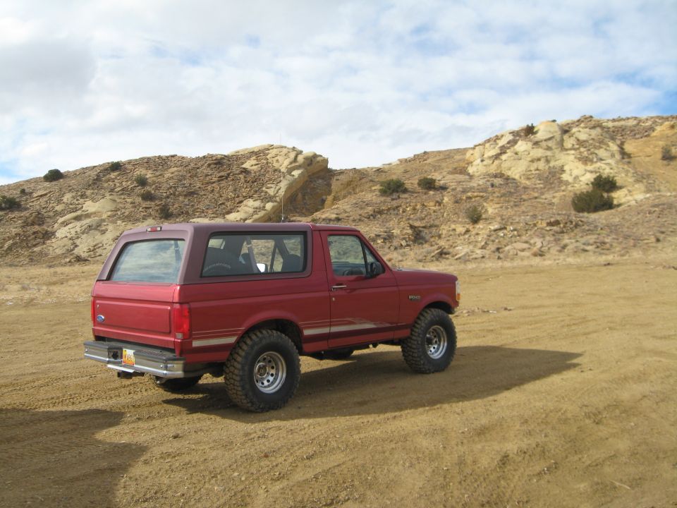 Red 1993 Ford Bronco parked on dirt road with rocky hills in background.