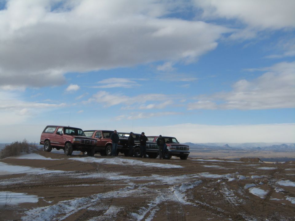 Four Ford trucks parked on a sandy, snow-dusted landscape.
