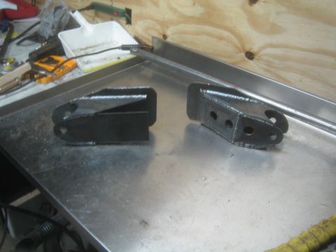 1990 Ford Bronco - Photograph of two fabricated steel suspension brackets on a shop bench, not a technical document.