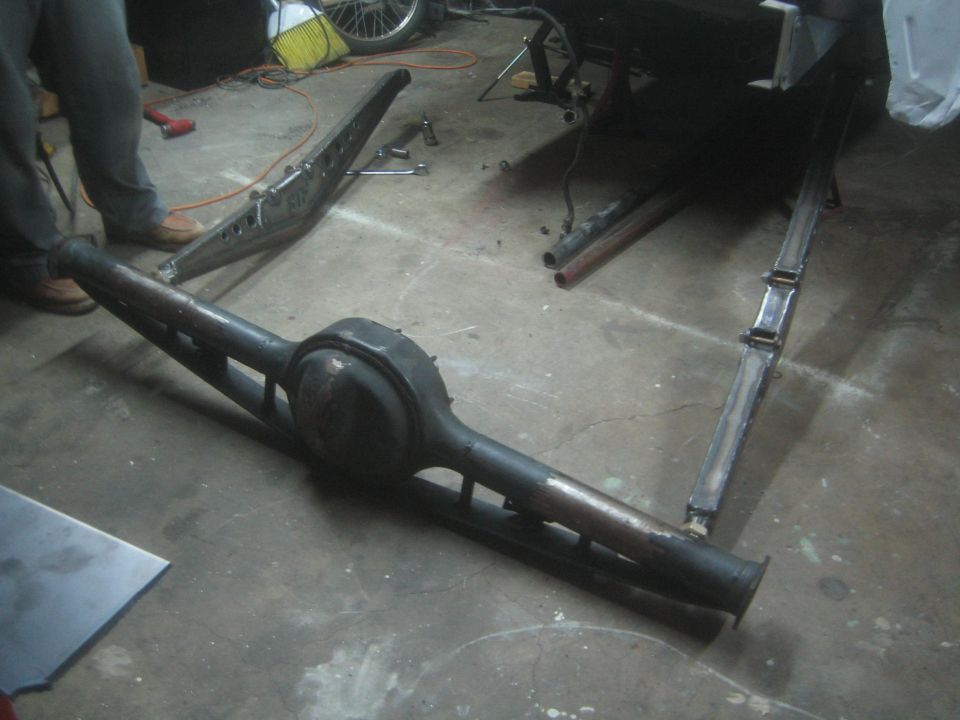 Fabricated axle housing and suspension links lying on a garage floor