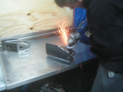 1990 Ford Bronco - Photograph of fabrication work: an angle grinder cutting a steel plate on a metal bench, not a technical document.