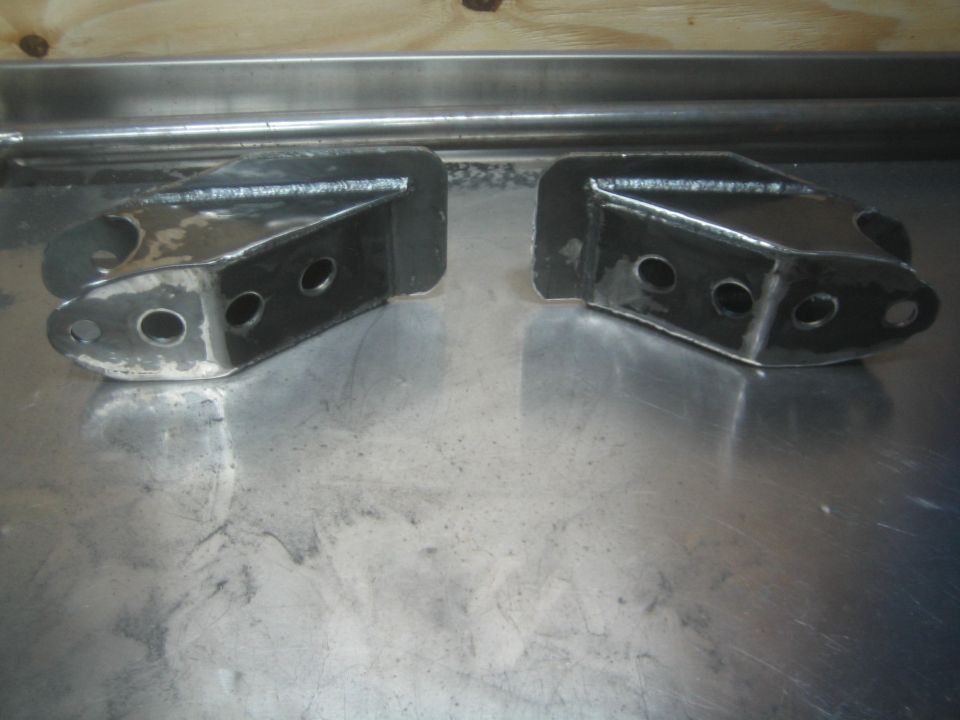 Two welded steel suspension brackets sitting on a metal table