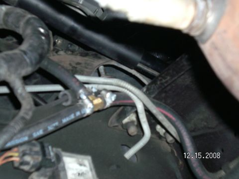 1996 Ford Bronco - Close-up underside/engine bay view showing rubber transmission hoses labeled 'MISSION SAE 30R6 MADE IN USA', a brass fitting with hex nuts…