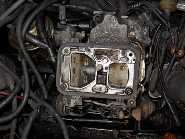 Close-up of a vehicle carburetor assembly with hoses and linkages.