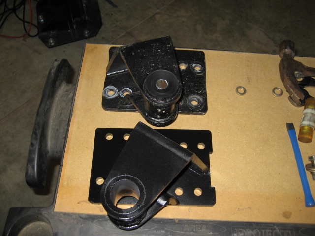 Two black metal brackets with rubber bushings on a wooden surface.