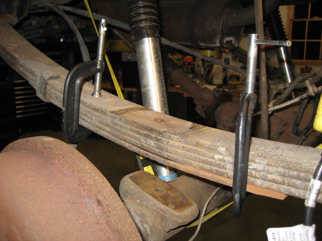 Close-up of C-clamps compressing a leaf spring on a vehicle suspension system.