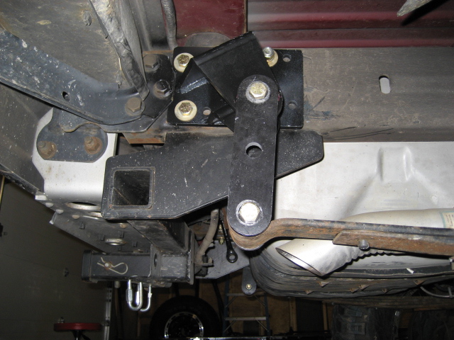 Underside of a vehicle showing a trailer hitch receiver and swing arm assembly.