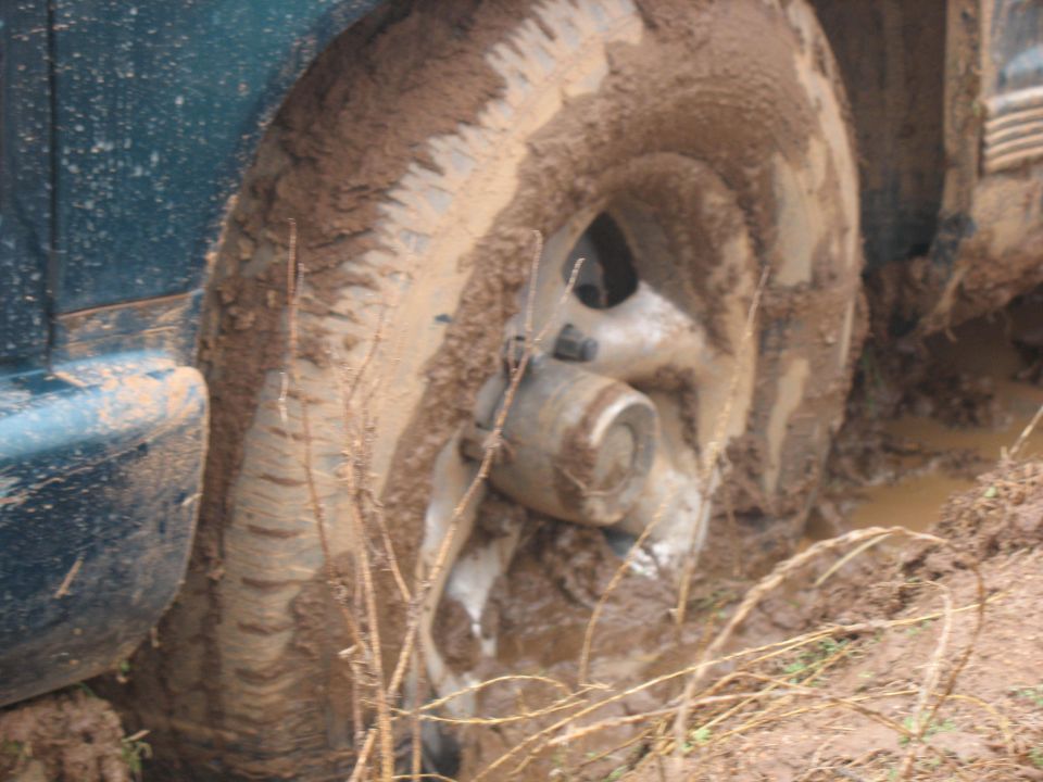 Mud-covered tire and teal fender of a vehicle stuck in mud.