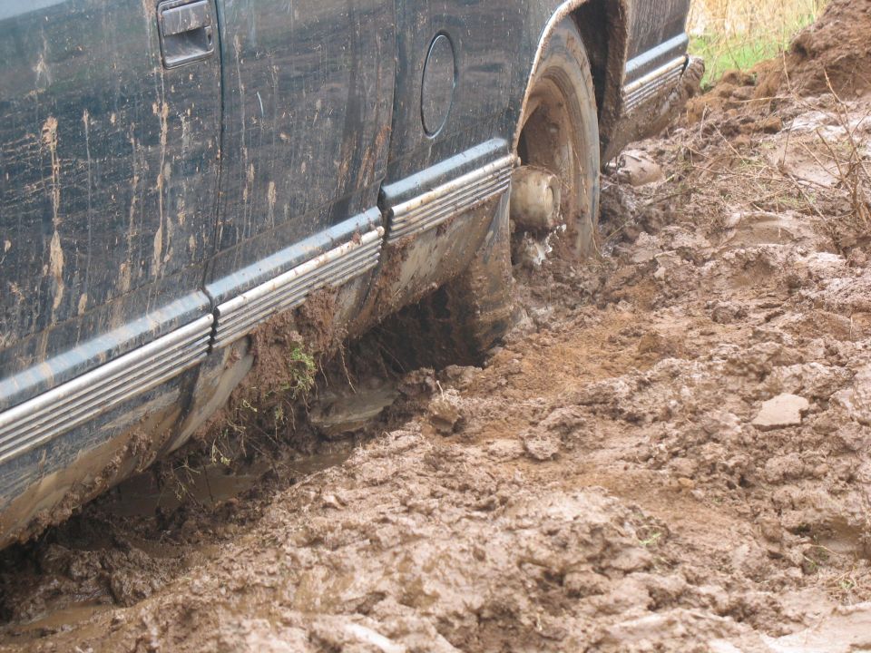 Dark-colored truck stuck in mud, driver's side door and rear wheel visible.