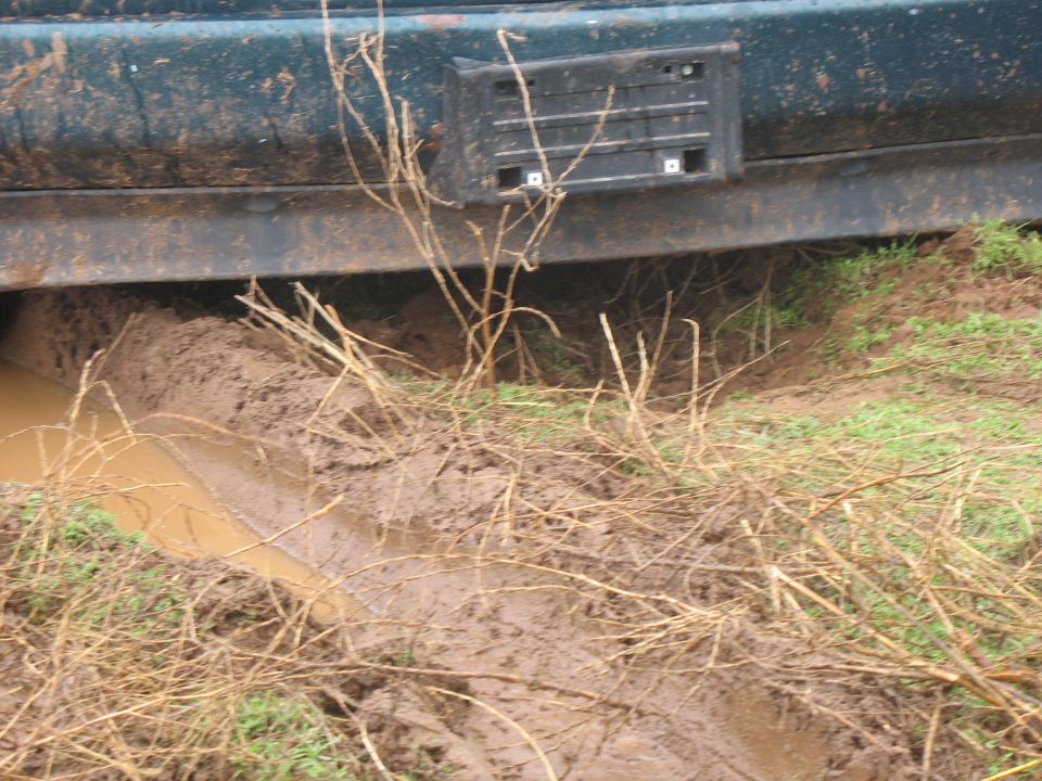 Dark green vehicle stuck in mud, showing rear bumper and lower body panel.