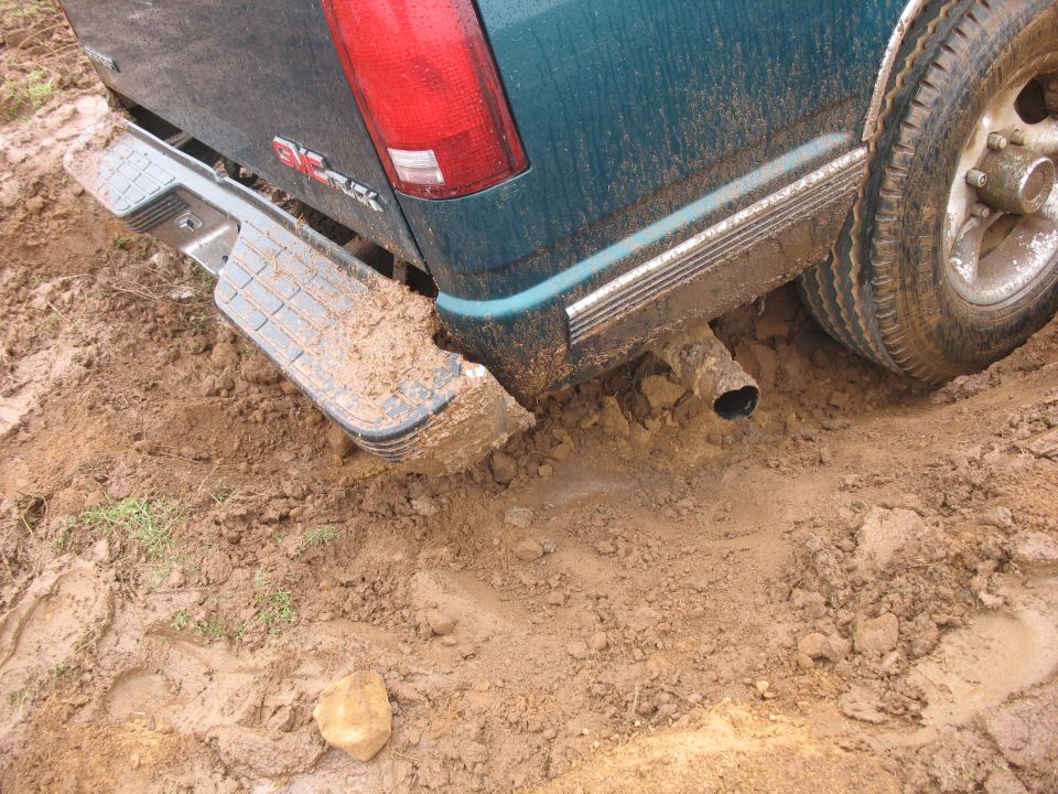 Teal pickup truck stuck in mud, showing rear bumper, exhaust, and tire.
