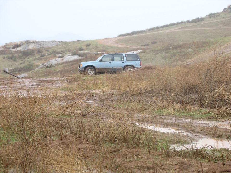 Blue SUV on a muddy off-road path with sparse vegetation.