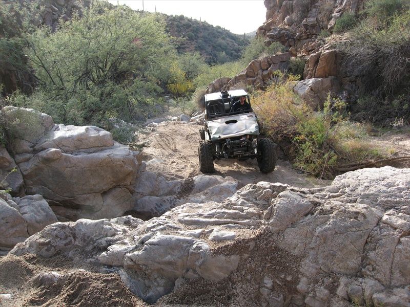 White off-road vehicle with large tires climbing over rocks in a desert wash.