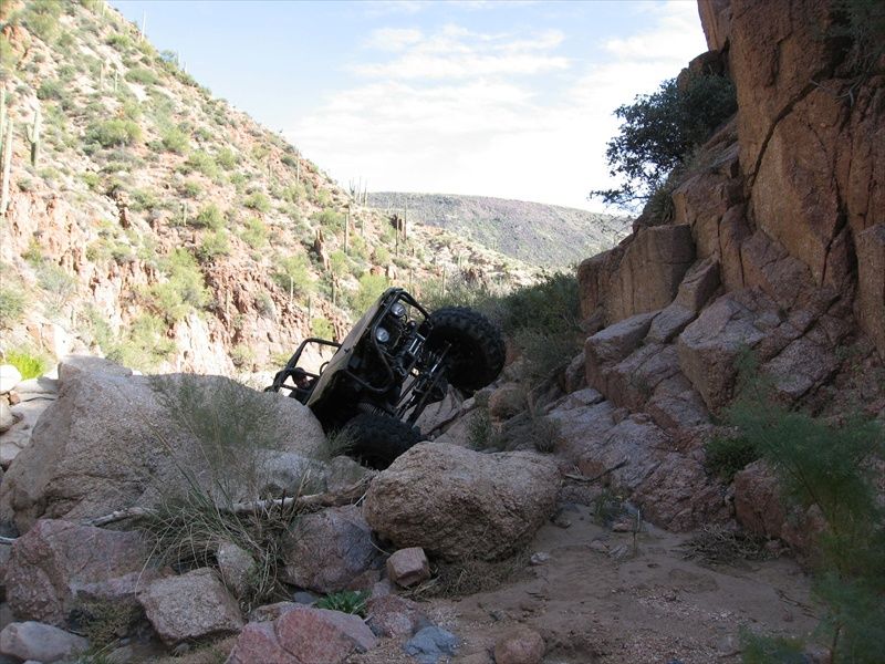 Black off-road vehicle tipped on its side in a rocky desert canyon.