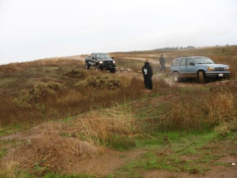 2001 Ford F-250 - A dark-colored Ford F-250 pickup truck is parked on a muddy, grassy hill under an overcast sky. A blue SUV is also visible further down the…
