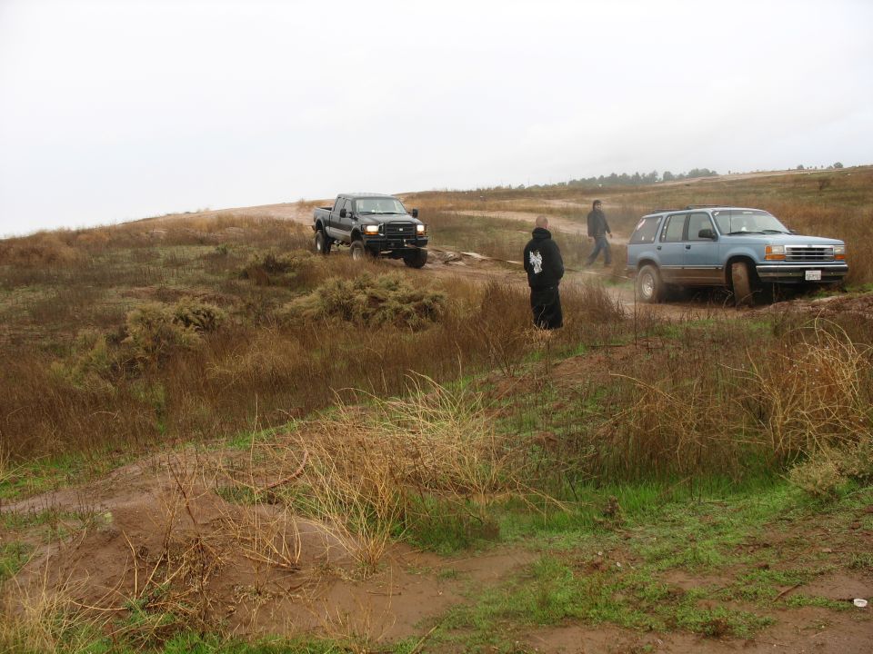 Dark Ford F-250 pickup truck on a muddy hill with a blue SUV and two people.
