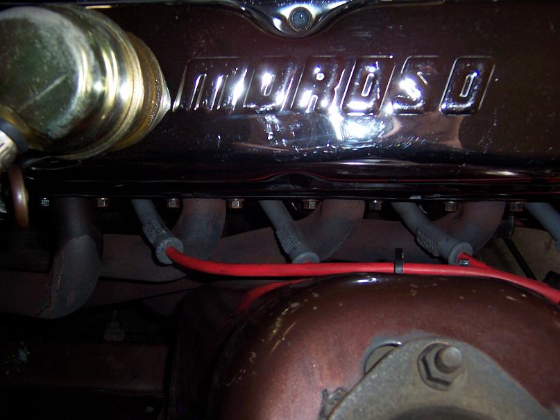 Chrome Moroso valve cover with red spark plug wire and exhaust manifold on inline engine