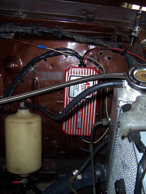 Red MSD 6AL ignition box mounted in brown engine bay near radiator and coolant overflow tank