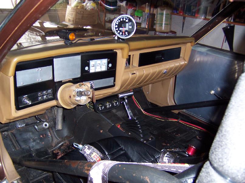 Interior of a modified vehicle with tan dashboard, tachometer, racing seat, and roll cage.