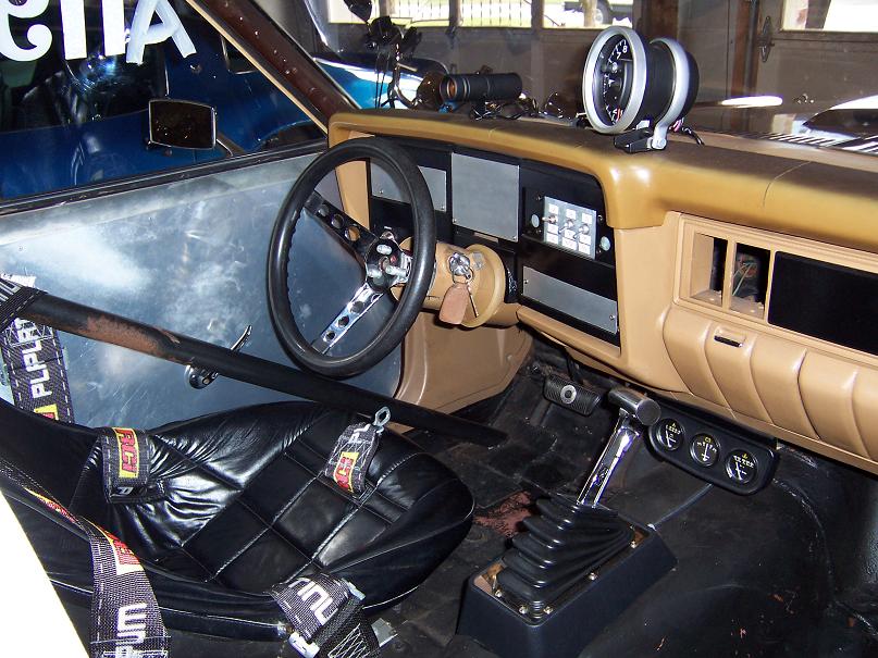 Interior of a modified car with racing seat, roll bar, custom steering wheel, and dashboard.