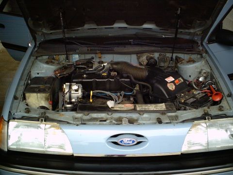 1986 Ford Taurus - The engine bay of a light blue 1986 Ford Taurus is visible with the hood raised, revealing the engine and other components.