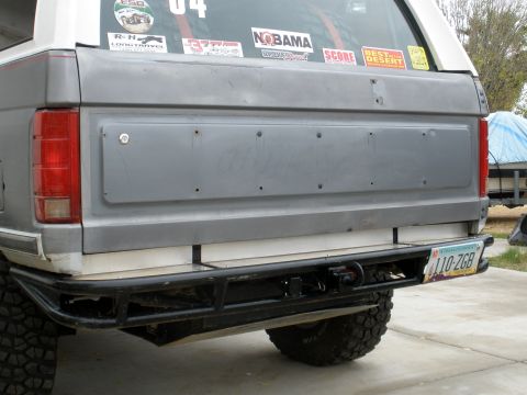 1980 Ford Bronco - The rear of a gray Ford Bronco is shown, featuring a black aftermarket bumper with a trailer hitch and an Arizona license plate reading "11…