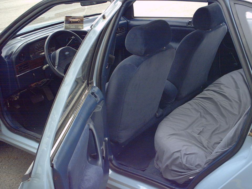 Blue cloth interior of a Ford sedan seen through the open rear door