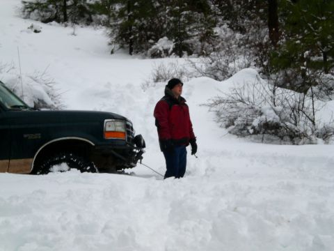 1995 Ford Bronco - A person stands next to a dark green Ford Bronco that is stuck in deep snow. The front of the SUV is visible, with its tires partially subm…