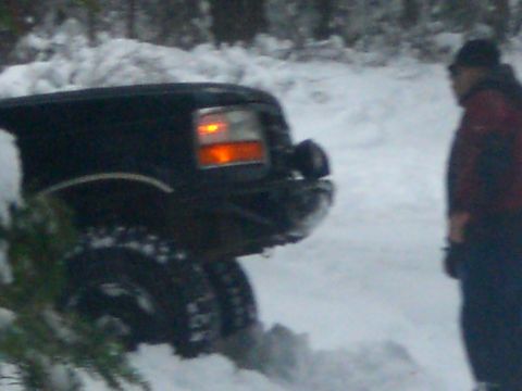 1995 Ford Bronco - A black Ford Bronco is partially visible in a snowy environment, with its rear tire and taillight illuminated. A person wearing a red and b…