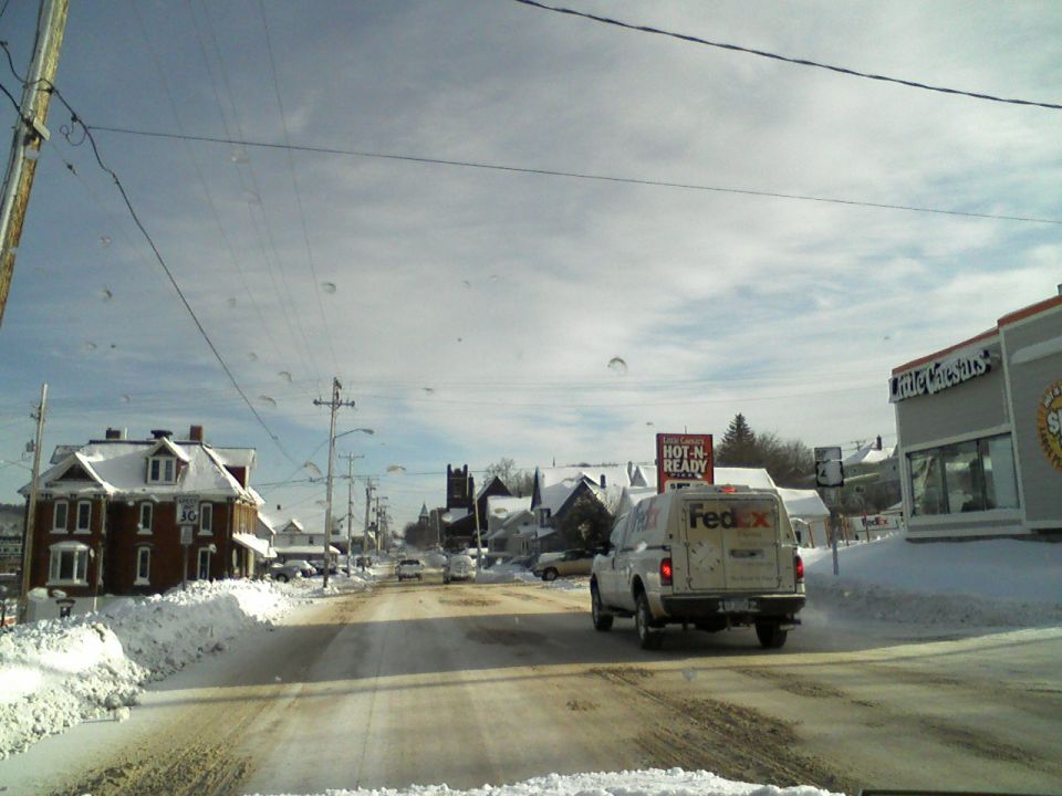 White Fedex van driving on a snowy road in a town.
