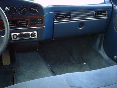 1986 Ford Taurus - The interior of a car shows blue carpeting and a dashboard with a stereo and air vents.