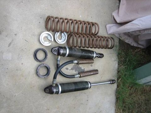 1984 Ford Bronco - Two sets of rear coil springs and two shock absorbers are laid out on a concrete surface next to some metal adjustment rings.