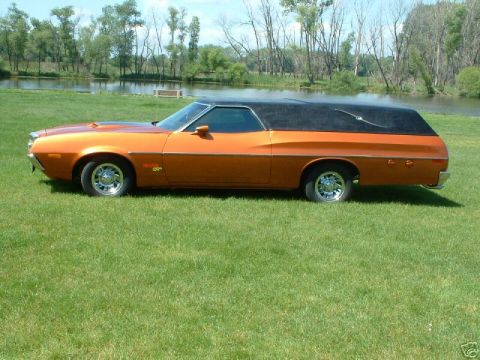 1972 Ford Ranchero - A side profile of an orange 1972 Ford Ranchero hearse with a black vinyl top is parked on a grassy lawn next to a body of water.