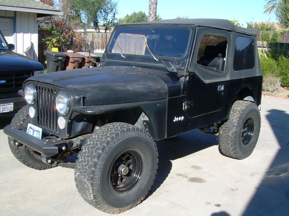 Black Jeep CJ-7 with soft top and off-road tires parked on a driveway.
